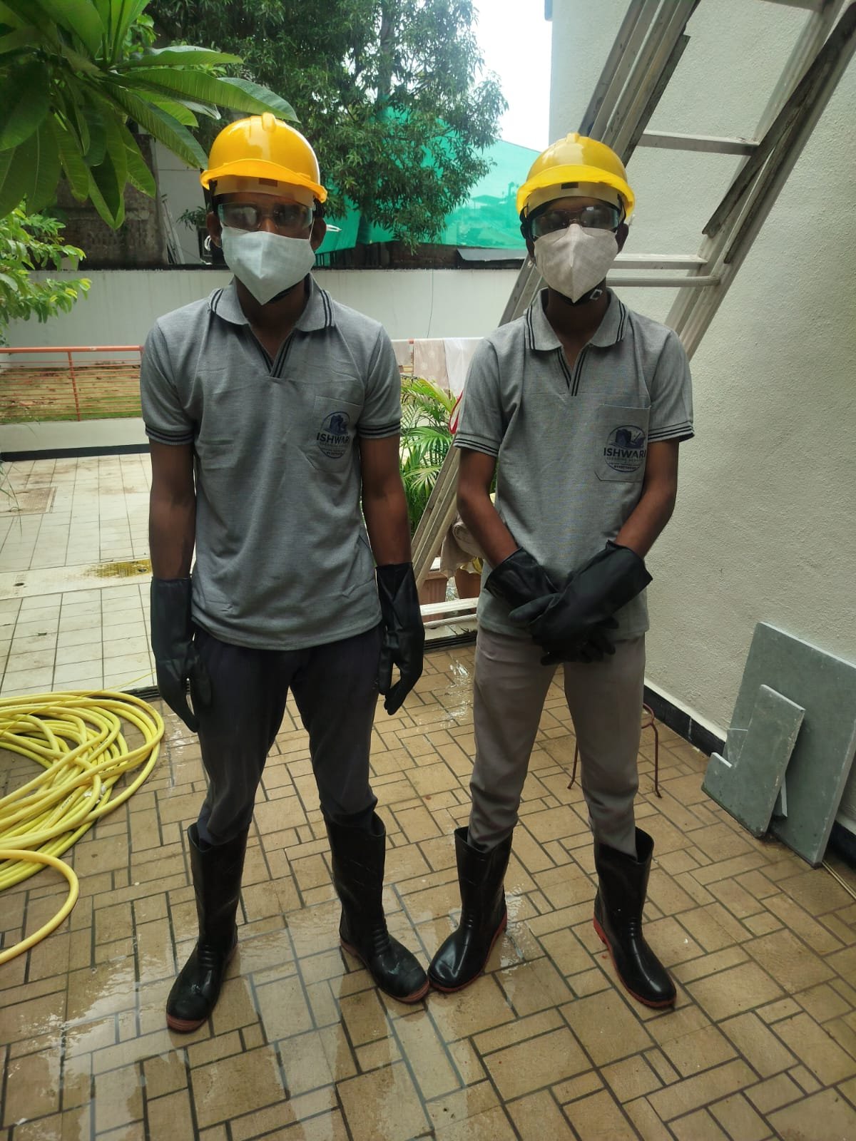 Two Ishwari cleaning professionals wearing helmets, masks, gloves and safety boots